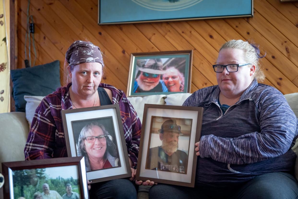 Meta Ross (left) and her sister, Sammi Ross, are shown with photos of their mom, Ginny Killam, and stepfather, Jeffery Killam. The spouses, both 59, died on Feb. 25.  (Robert Short/CBC - image credit)