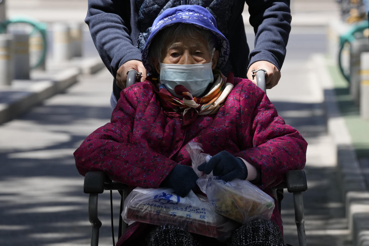 FILE - An elderly resident wearing mask is pushed in a wheelchair as she carries take away food on Friday, May 13, 2022, in Beijing. (AP Photo/Ng Han Guan, File)