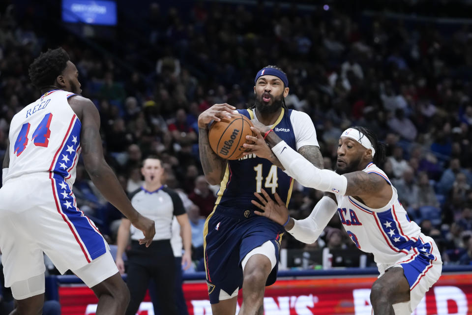 New Orleans Pelicans forward Brandon Ingram (14) is fouled as he drives to the basket between Philadelphia 76ers forward Paul Reed (44) and forward Robert Covington in the first half of an NBA basketball game in New Orleans, Wednesday, Nov. 29, 2023. (AP Photo/Gerald Herbert)