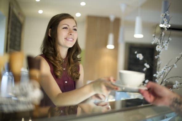 young woman working in a coffee shop hands over the cup