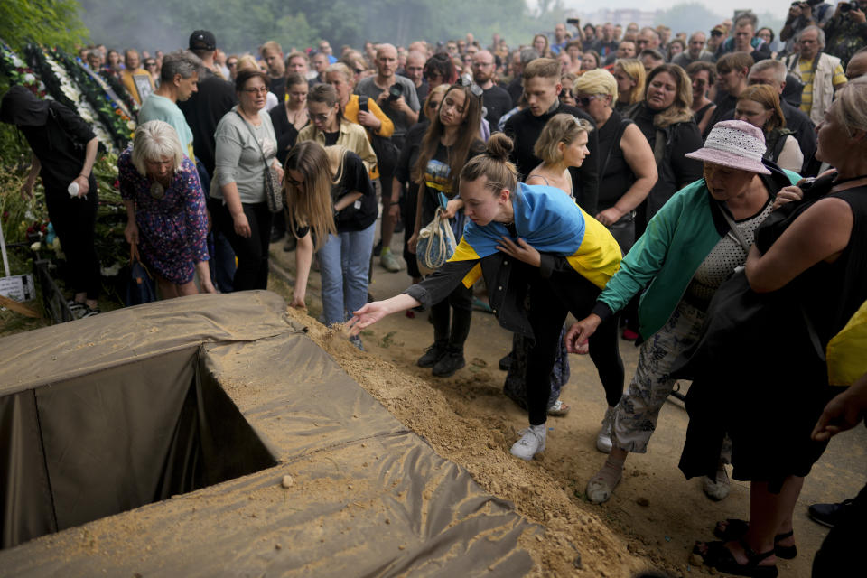 People throw sand on the coffin with the remains of activist and soldier Roman Ratushnyi during his funeral in Kyiv, Ukraine, Saturday, June 18, 2022. Ratushnyi died in a battle near Izyum, where Russian and Ukrainian troops are fighting for control of the area. (AP Photo/Natacha Pisarenko)