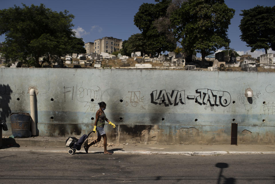 A woman wearing a face mask and gloves walks past Nossa Senhora das Gracas cemetery during the COVID-19 pandemic in Duque de Caxias, Rio de Janeiro, Brazil, Monday, April 27, 2020. (AP Photo/Silvia Izquierdo)