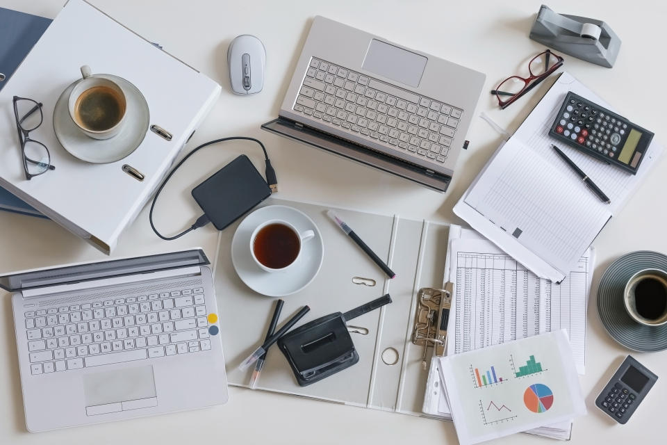 Top view of a full business desk with laptops, accounting papers, calculator, coffee and other office supplies