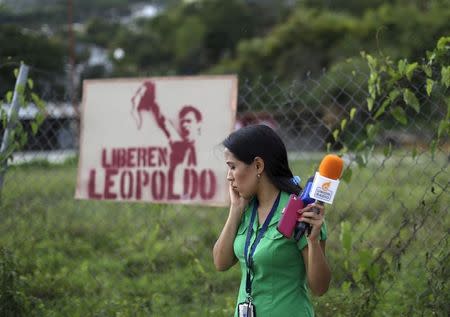 A journalist speaks on her cellphone in front of a sign with the image of jailed Venezuelan opposition leader Leopoldo Lopez outside the prison of Ramo Verde, on the outskirts of Caracas, June 18, 2015. REUTERS/Jorge Dan Lopez