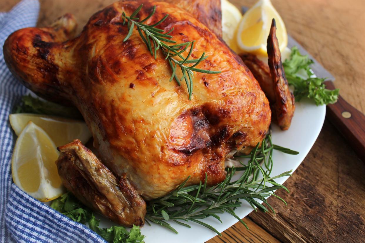 Closeup of simple roast chicken with lemons and herbs on a white plate with a knife on a wooden table