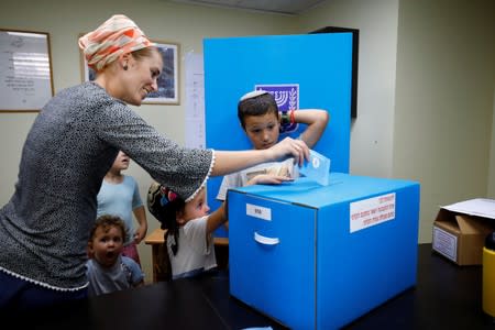 A woman casts her vote in a ballot box as children watch during Israeli's parliamentary election, at a polling station in the Israeli settlement of Adora, in the occupied West Bank