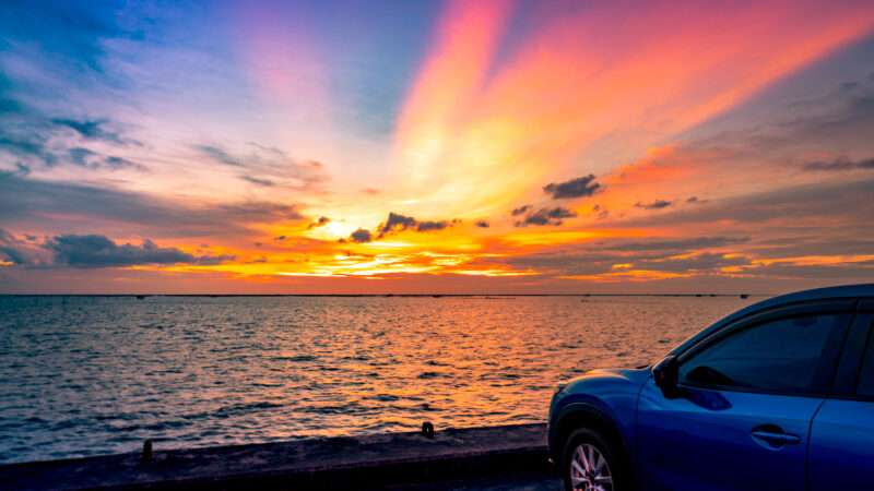 A compact blue car parked at the beach overlooking a picturesque sunset.