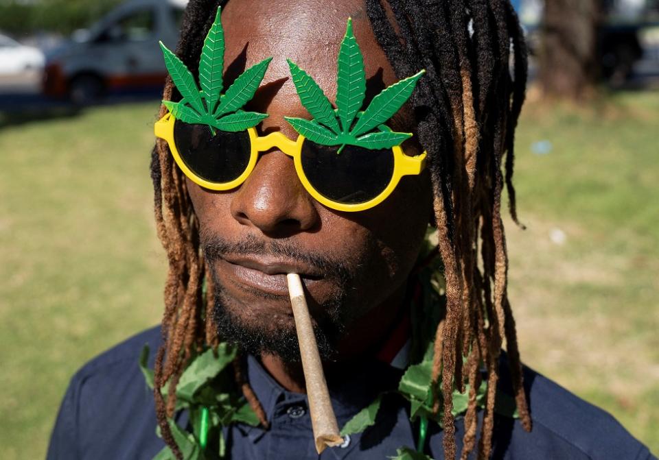 A man holds a cannabis cigarette in his mouth at the protest in Johannesburg. He is wearing yellow sunglasses with a big, green, marijuana leaf motif.