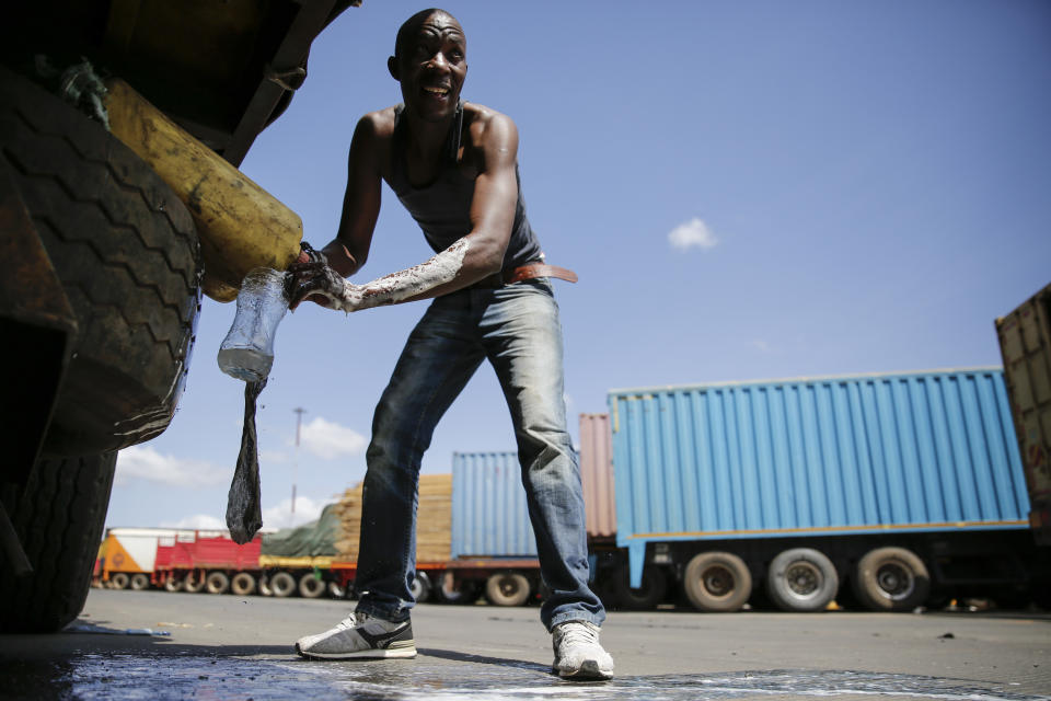 In this photo taken Monday, June 1, 2020, Tanzanian truck driver Ally Akida Samwel washes his hands next to his truck as he waits to be allowed to enter on the Kenya side of the Namanga border crossing with Tanzania. Africa's long-haul truckers carry food, fuel and other essential supplies along dangerous roads, but now they say they are increasingly accused of carrying the coronavirus as well. The drivers say they are stigmatized and even threatened in some countries. (AP Photo/Brian Inganga)