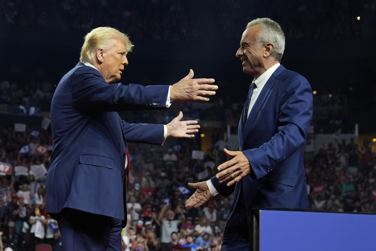 Donald Trump extends arms toward Robert F. Kennedy Jr. onstage.