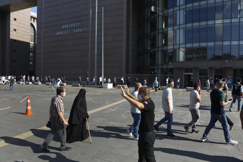 A police officer gives instructions to people to observe social distancing, as people walk outside a court in Istanbul, Friday, July 3, 2020, where the trial began for defendants accused of smuggling former Nissan Motor Co. chairman Carlos Ghosn out of Japan. A private airline official, four pilots and two flights attendants are on trial in Istanbul, accused of smuggling former Nissan Motor Co. chairman Carlos Ghosn out of Japan to Lebanon, via Turkey. Turkish prosecutors are seeking up to eight years in prison each for the four pilots and the airline official on charges of illegally smuggling a migrant, for helping Ghosn escape to Lebanon while he awaited trial in Japan. (AP Photo/Mehmet Guzel)