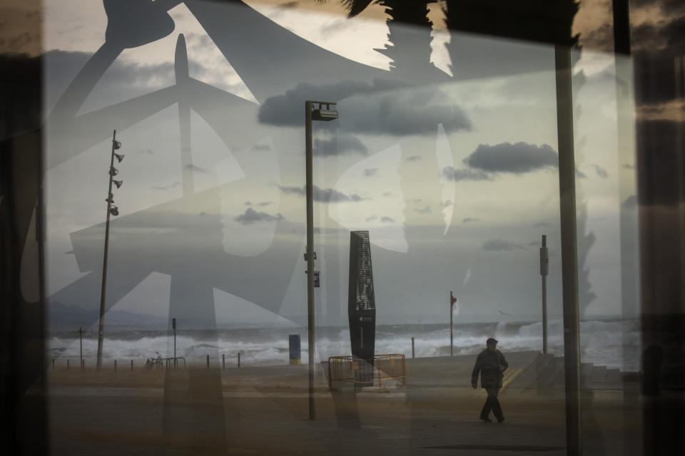 A man is seen through a window as he walks near the beach during strong winds in Barcelona, Spain, Monday, Jan. 20, 2020. Two people have died as storms carrying heavy snowfalls and gale-force winds lashed many parts of Spain on Monday. The storm has forced the closure of Alicante airport and some 30 roads in eastern region. Six provinces are on top alert. (AP Photo/Emilio Morenatti)