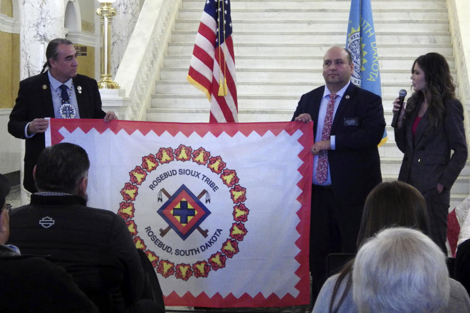 South Dakota state Democratic Sen. Shawn Bordeaux, left, and Rep. Eric Emery hold the flag of the Rosebud Sioux Tribe on Wednesday, Jan. 10, 2024, at the state Capitol in Pierre, S.D. At right is South Dakota Republican Gov. Kristi Noem. (AP Photo/Jack Dura)