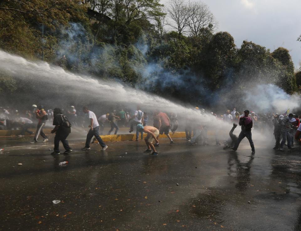 Manifestantes tratan de protegerse de chorros de agua lanzada por vehículos de la policía antimotines en una protesta antigubernamental en Caracas, Venezuela, el miércoles 12 de marzo de 2014. (AP Photo/Fernando Llano)