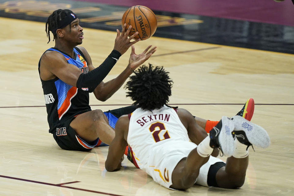 Oklahoma City Thunder's Shai Gilgeous-Alexander, left, passes the ball as Cleveland Cavaliers' Collin Sexton watches in the first half of an NBA basketball game, Sunday, Feb. 21, 2021, in Cleveland. (AP Photo/Tony Dejak)