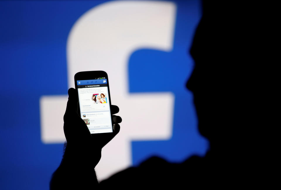 A man is silhouetted against a video screen with a Facebook logo as he poses with a Samsung S4 smartphone in this photo illustration taken in the central Bosnian town of Zenica, August 14, 2013. REUTERS/Dado Ruvic/File Photo