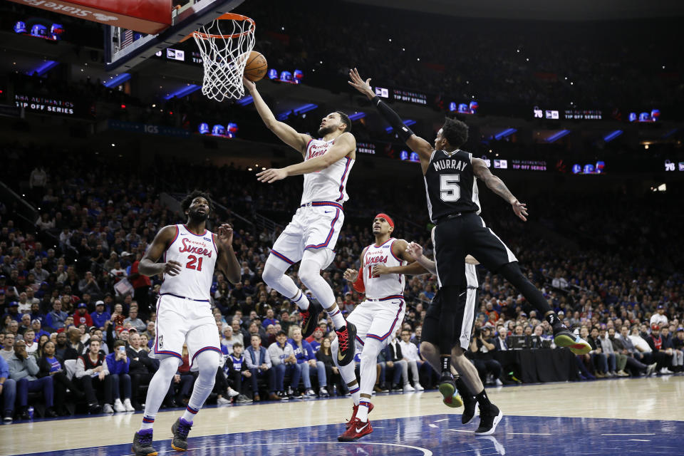 Philadelphia 76ers' Ben Simmons, center, goes up for a shot past San Antonio Spurs' Dejounte Murray, right, during the first half of an NBA basketball game Friday, Nov. 22, 2019, in Philadelphia. (AP Photo/Matt Slocum)