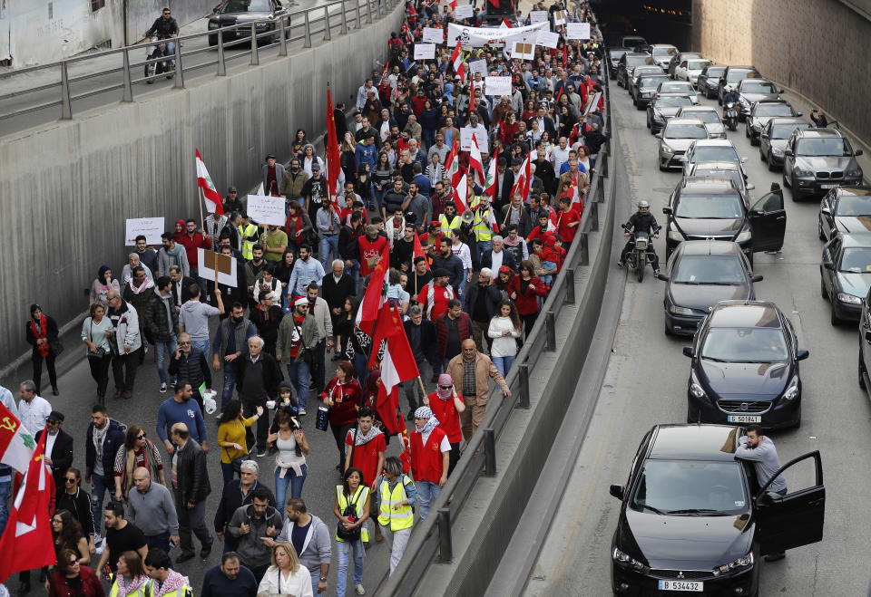 People stand outside their cars watching an anti-government march organized by the country's communist party, in Beirut, Lebanon, Sunday, Dec. 16, 2018. Hundreds of Lebanese called for an end to a stalemate over forming a government seven months after elections. The Sunday protests were organized by the country's vibrant communist party, but drew others frustrated by the country's deepening economic and political crisis. (AP Photo/Hussein Malla)