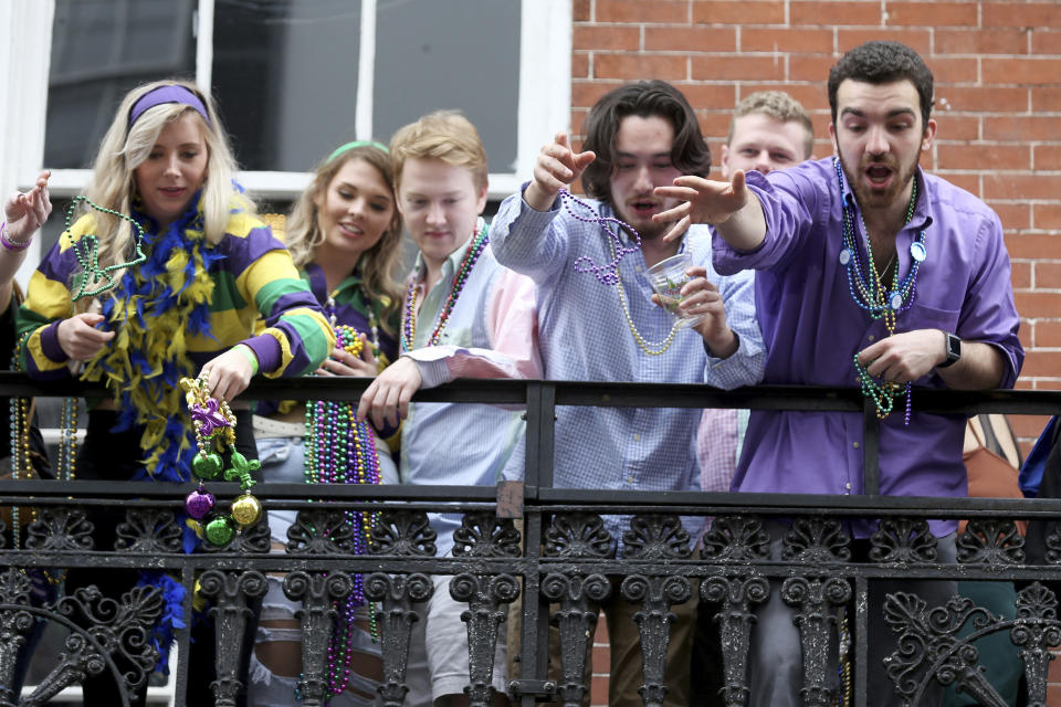 FILE - In this Tuesday, Feb. 25, 2020, file photo, a group of revelers on a balcony toss beads to the crowd below on Bourbon Street on Mardi Gras day in New Orleans. A month ago, the streets were awash in people and the city was steeped in its most cherished tradition of communal joy: Carnival season was nearing its Mardi Gras climax, with parades rolling, beer flowing and money changing hands at bars and restaurants. But now since the coronavirus outbreak, the bars are closed and restaurants struggle with take-out- or delivery-only operations — the ones that stay open. (AP Photo/Rusty Costanza, File)