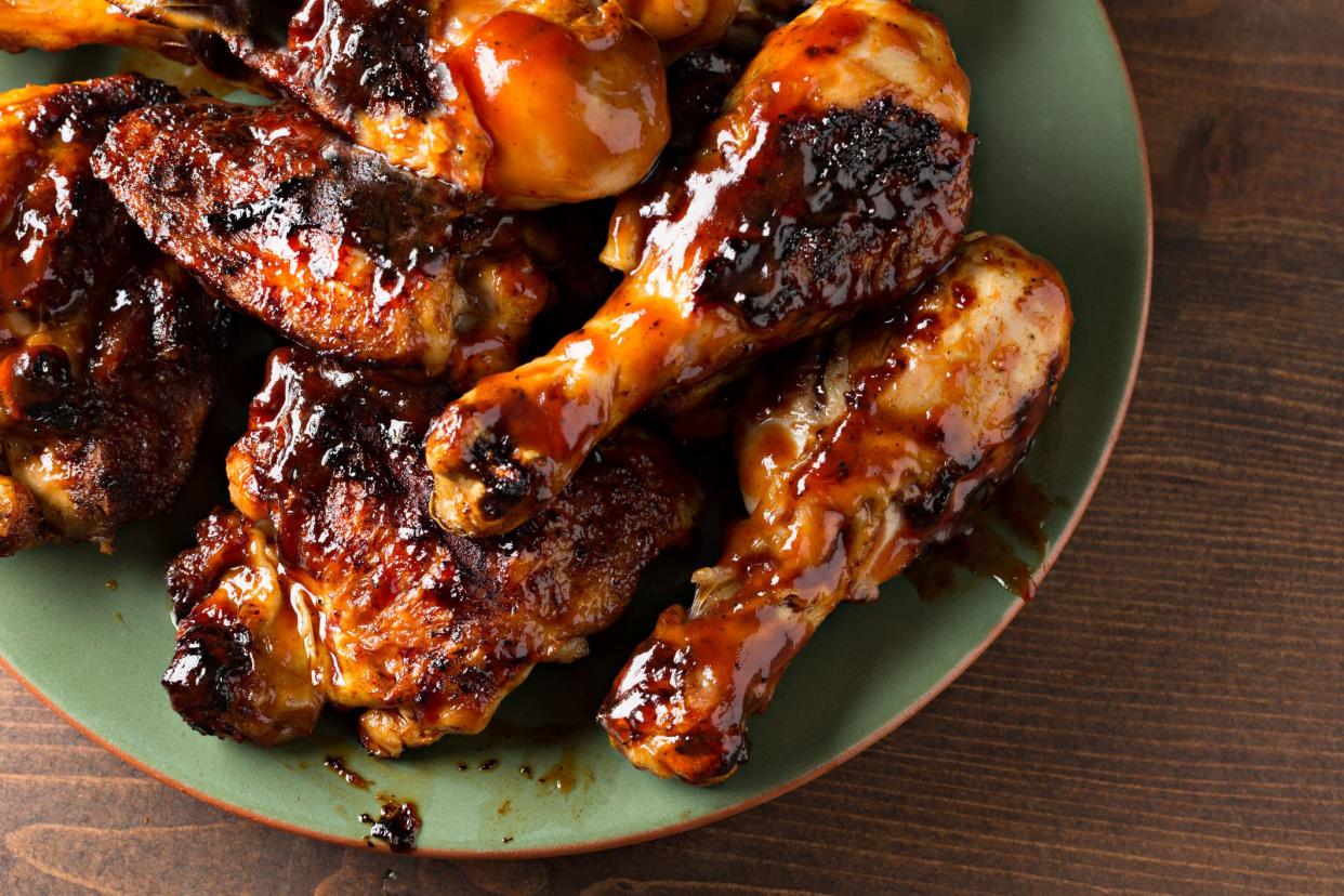 A high angle extreme close up horizontal photograph of some barbecued chicken drumsticks and thighs on a green platter.