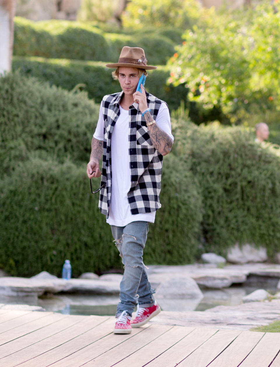 In between hanging out with his crew including the Jenner sisters, Hailey Baldwin, and Nash Grier, Justin Bieber took a phone call wearing a Nick Fouquet hat, distressed denim pants, a sleeveless gingham shirt, and red sneakers.