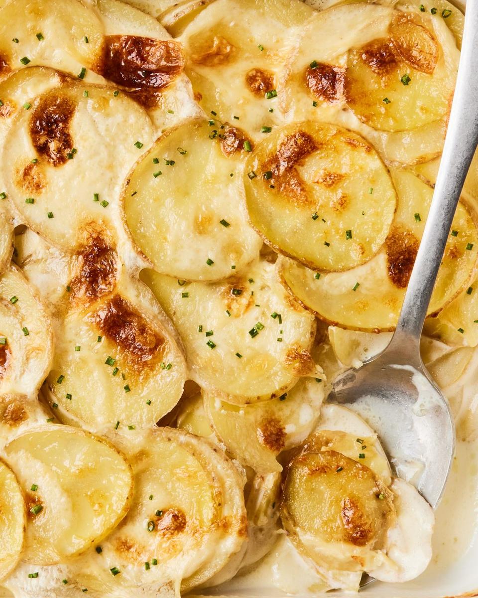 scalloped potatoes in a white baking dish with a silver serving spoon