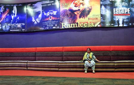 A poster for the movie "Waar" (2nd L) hangs near a woman sitting a on couch in the lobby of Atrium cinemas in Karachi, ahead of the movie's screening, October 23, 2013. REUTERS/Akhtar Soomro