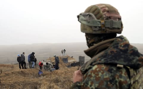 A Ukrainian serviceman looks on as volunteers dig trenches on the coast of the Sea of Azov near Mariupol - Credit: SEGA VOLSKII/ AFP