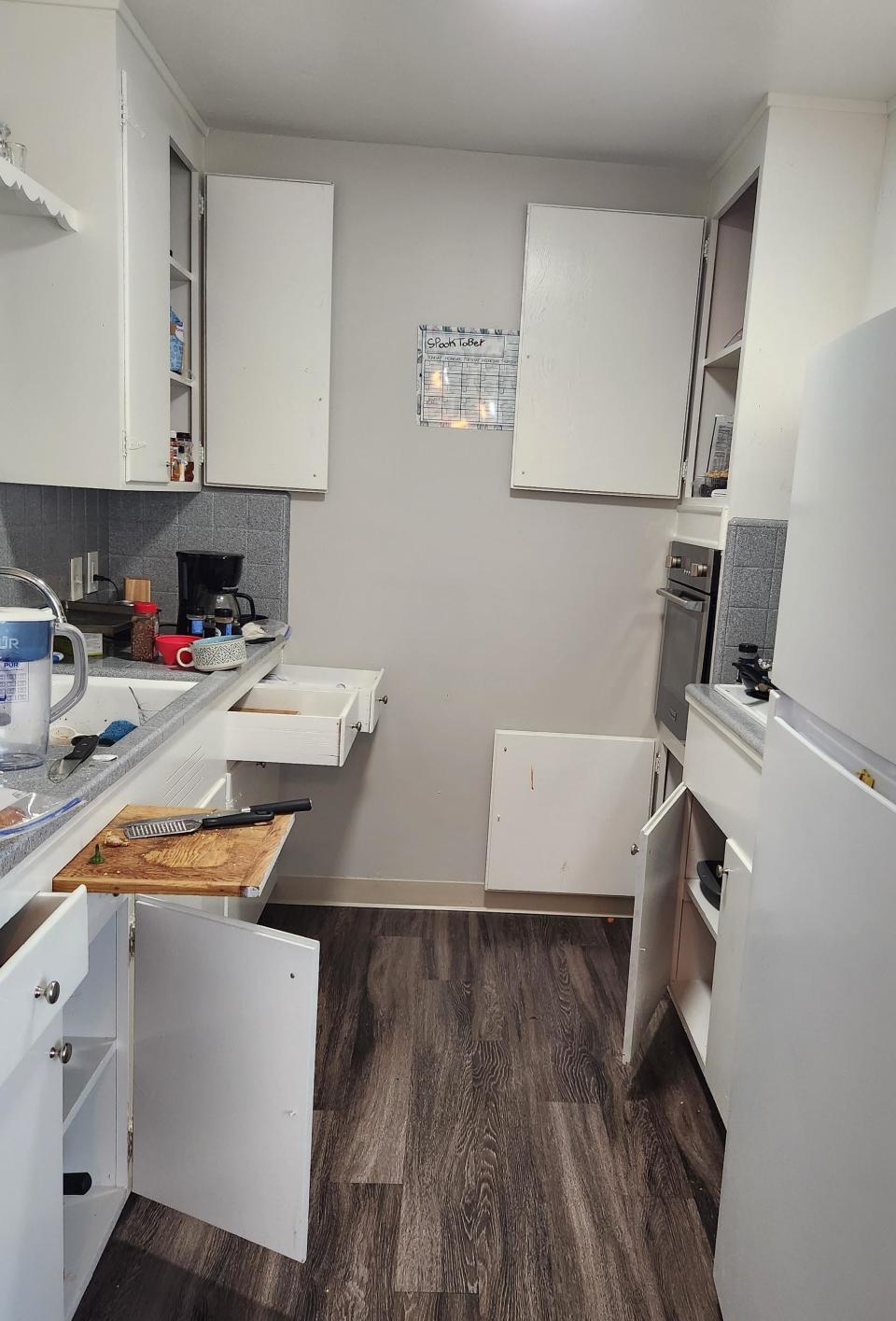 A small kitchen with open drawers and cabinets, appliances on countertops, and items scattered about