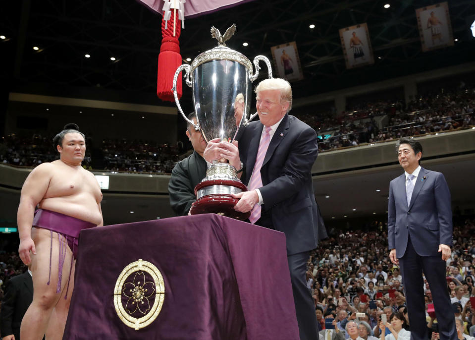 President Donald Trump, center, lifts the "President's Cup" trophy to present to the Tokyo Grand Sumo Tournament winner Asanoyama, left, at Ryogoku Kokugikan Stadium, Sunday, May 26, 2019, in Tokyo. Japanese Prime Minister Shinzo Abe is at right. (Daiki Katagiri/Kyodo News via AP)