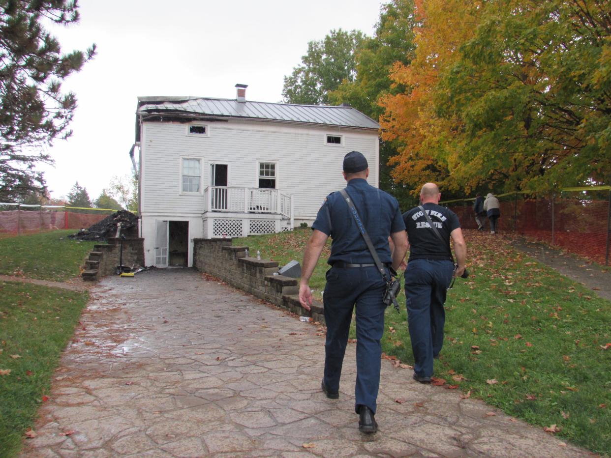 Two firefighters walk toward Heritage House on Sunday in Stow. Significant damage was sustained by the historic building in a fire.