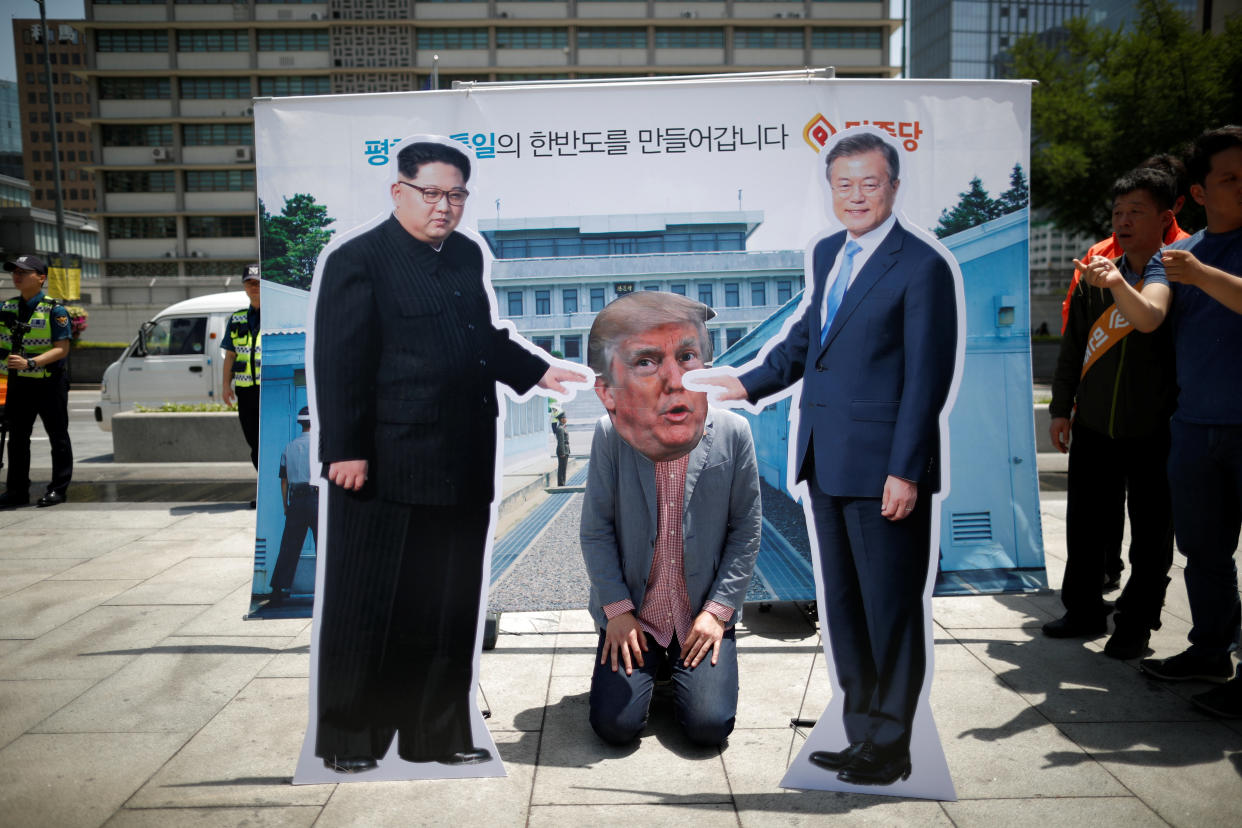 A man wearing a Trump mask kneels between cutouts of North Korean leader Kim Jong Un and South Korean President Moon Jae-in during an anti-Trump rally in Seoul, South Korea, on May 25, 2018.&nbsp; (Photo: Kim Hong-Ji / Reuters)