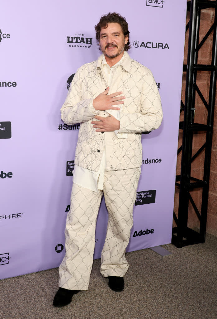 Pedro Pascal posing at an event in a patterned suit with hands crossed over his chest