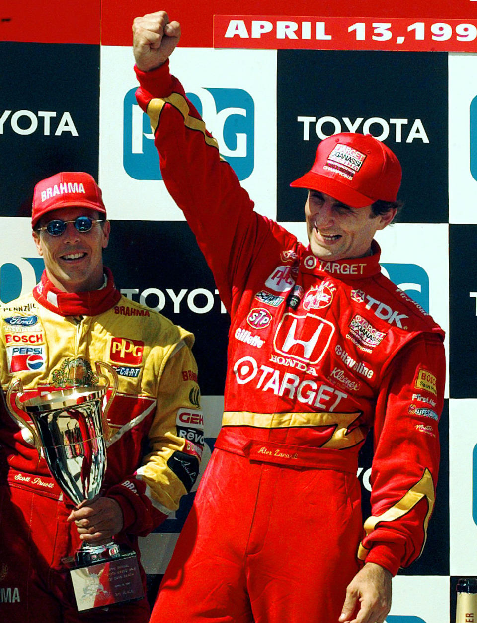 FILE - In this April 13, 1997, file photo, Italian driver Alex Zanardi raises his fist while he celebrates his victory at the Toyota Grand Prix of Long Beach in Long Beach, Calif. Third place finisher Scott Pruett, of Crystal Bay, Nev., is at left holding his trophy. Every now and then Alex Zanardi has a chance encounter with someone who reminds him there’s never any reason to feel sorry for himself, not that he ever had during his two vastly different lifetimes: the one with legs, and the other as a double-amputee. (AP Photo/Kevork Djansezian, File)
