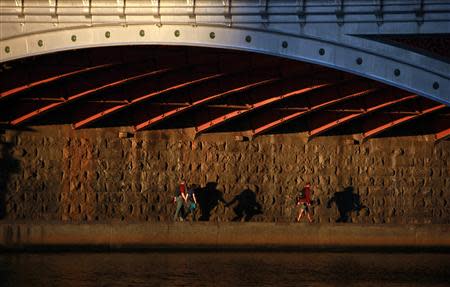 Pedestrians cast shadows as they walk under a bridge along a footpath on the banks of Melbourne's Yarra River at sunset in this January 16, 2013 file photo. REUTERS/David Gray/Files