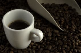 Double espresso cup of coffee against blended coffee beans and measure scoop background.