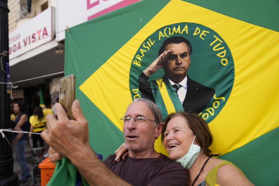 Supporters of Brazilian President Jair Bolsonaro pose for photos in front of his image during a re-election campaign rally in Juiz de Fora, Minas Gerais state, Brazil, Tuesday, Aug. 16, 2022. Bolsonaro formally began his campaign for re-election in this town where he was stabbed during his 2018 campaign. General elections are set for Oct. 2. (AP Photo/Silvia Izquierdo)