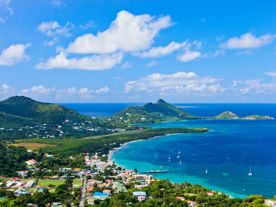 An aerial view of the island of Grenada, with blue water lining a sandy beach and verdant green shore.