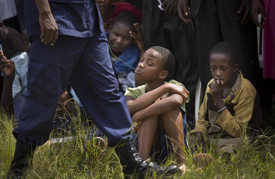 In this photo taken Thursday, March 27, 2014, young boys listen to genocide memories and observe a flame of remembrance, at a ceremony in the town of Kirehe, eastern Rwanda. Rwandans gathered under spittles of rain Thursday to watch the arrival of a small flame, symbolic fire traveling the country as Rwanda prepares to mark 20 years since ethnic Hutu extremists killed neighbors, friends and family during a three-month rampage of violence aimed at ethnic Tutsis and some moderate Hutus, the death toll of which Rwanda puts at 1,000,050. (AP Photo/Ben Curtis)