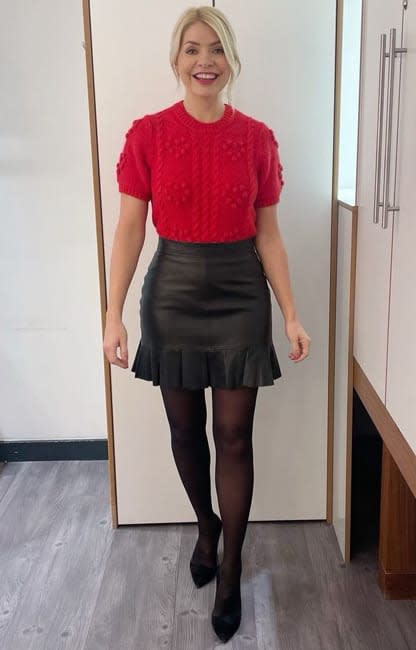 holly poses in a leather mini skirt and red top