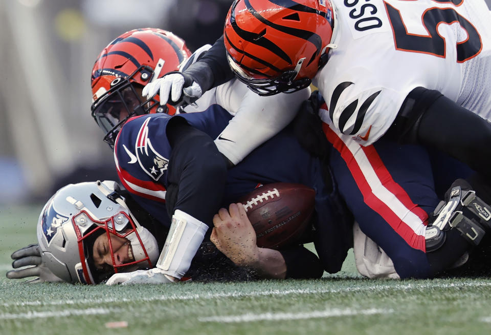 New England Patriots quarterback Mac Jones, left, holds the ball as he hits the ground while Cincinnati Bengals defensive end Joseph Ossai, right, defends during the second half of an NFL football game, Saturday, Dec. 24, 2022, in Foxborough, Mass. (AP Photo/Michael Dwyer)