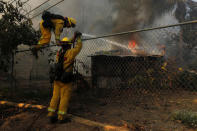 Firefighters jump a fence to try and save a burning home from the Lilac Fire, a fast moving wild fire, came through Bonsall, California, U.S., December 7, 2017. REUTERS/Mike Blake