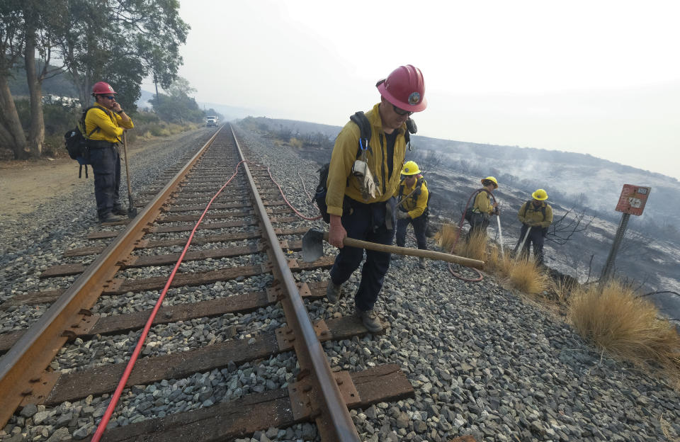 A crew with the County of Santa Barbara Fire Department firefighters extinguishes walks along railroad tracks parallel to the U.S. 101 highway Wednesday, Oct. 13, 2021, in Goleta, Calif. A wildfire raging through Southern California coastal mountains threatened ranches and rural homes and kept a significant highway shut down Wednesday as the fire-scarred state faced a new round of dry winds that raised risk of flames. The Alisal Fire covered more than 22 square miles (57 square kilometers) in the Santa Ynez Mountains west of Santa Barbara, and the number of firefighters was nearly doubled to 1,300, with more on the way. (AP Photo/Ringo H.W. Chiu)