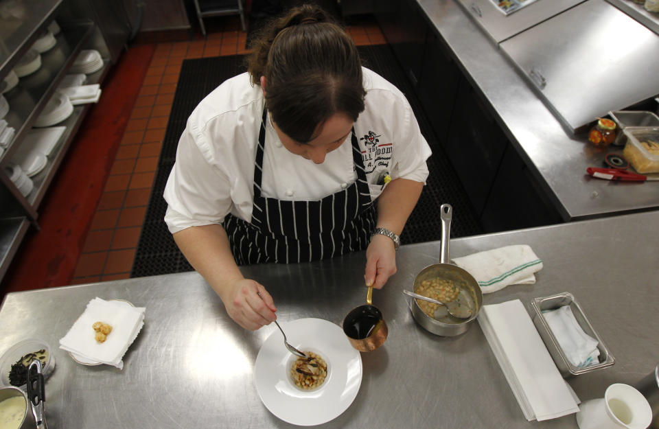 In this Dec. 7, 2012 photo, executive chef Kristin Butterworth prepares her braised pork belly with gulf shrimp, white bean cassoulet, garlic jus and fried baby sage, at the Grill Room of the Windsor Court Hotel in New Orleans. Roughly 50 restaurants in New Orleans are reviving an old Creole custom called reveillon, which stems from the old French tradition of eating a lavish meal after midnight Mass on Christmas Eve. (AP Photo/Gerald Herbert)