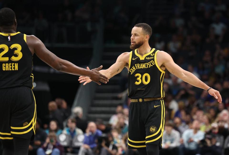 Golden State Warriors guard Steph Curry, right, reaches out to slap hands with teammate Draymond Green, left, following a play against the Charlotte Hornets during first quarter action at Spectrum Center in Charlotte, NC on Friday, March 29, 2024. JEFF SINER/jsiner@charlotteobserver.com