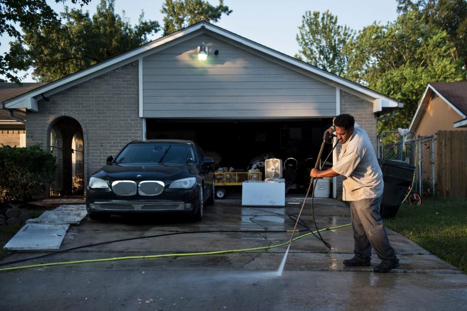 A man power-washes the driveway&nbsp;of his once flooded home.