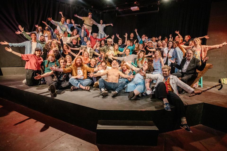 Big group of people posing with hands raised on a stage