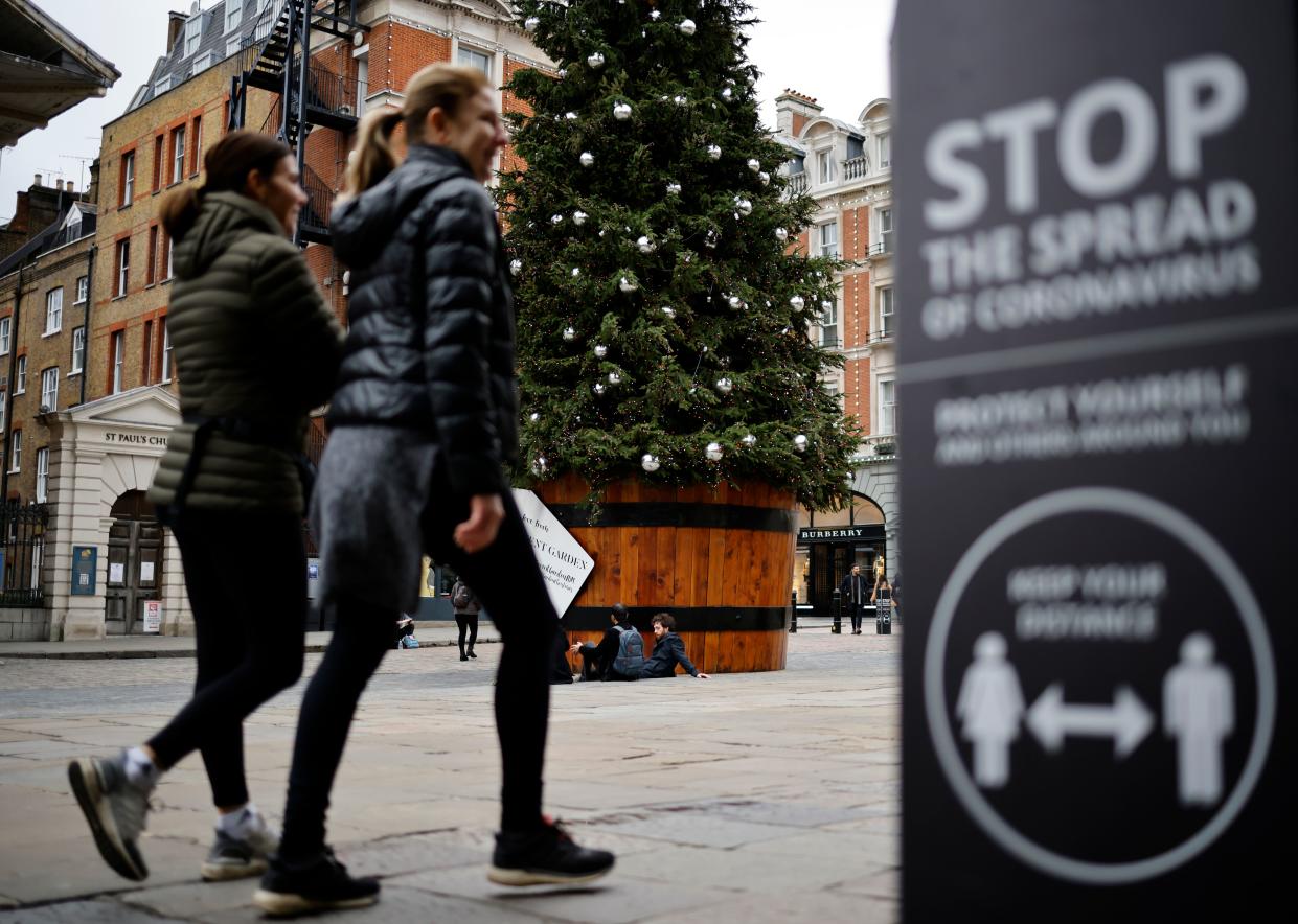 Pedestrians pass a COVID-19 sign reading "Stop the spread" as they walk past a Christmas tree in Covent Garden in central London on November 17, 2020. - Britain has been the worst-hit nation in Europe recording more than 50,000 coronavirus deaths from some 1.2 million positive cases. (Photo by Tolga AKMEN / AFP) (Photo by TOLGA AKMEN/AFP via Getty Images)