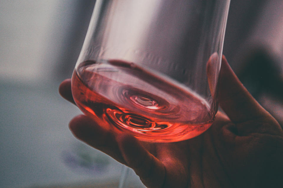 Hand holding a clear glass with a small amount of liquid, possibly for a health-related topic