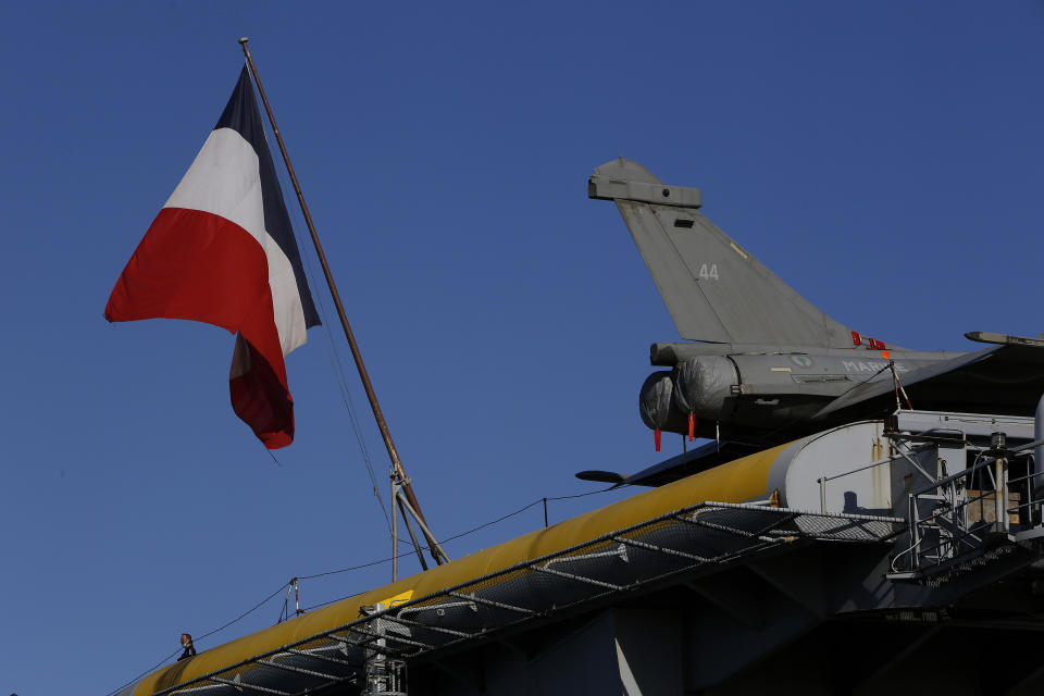 A French crew member stands next of a French flag and an aircraft on the France's nuclear-powered aircraft carrier Charles de Gaulle at Limassol port, Cyprus, Monday, May 10, 2021. With the Task Force's deployment on its mission named "Clemenceau 21," France is assisting in the fight against terrorism while projecting its military power in regions where it has vital interests. (AP Photo/Petros Karadjias)